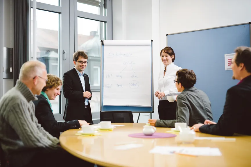 Eine Gruppe Menschen sitzt und steht um einen Tisch herum und bespricht sich