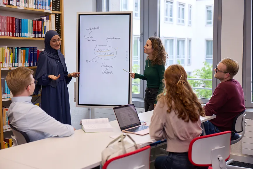 Eine Gruppe Studierender macht eine Gruppenarbeit in einer Bibliothek