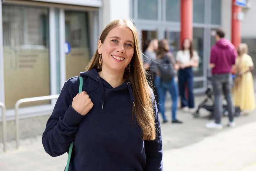 Eine Studierende steht vor dem Eingang der EVHN, wo sich einige andere Studierende unterhalten