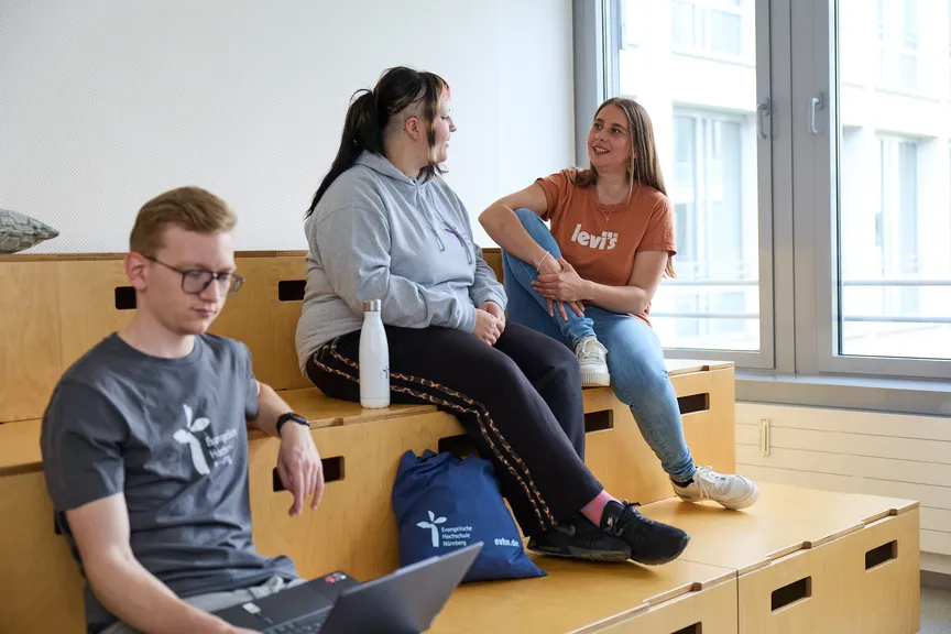 Einige Studierende sitzen auf einer hölzernen Sitzgelegeneheit