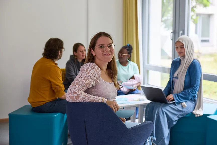 Eine Studierende sitzt vor einer Gruppe anderer Studierender und lächelt in die Kamera
