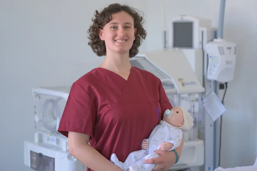 Eine Studierende in einem Kasak hält eine Simulationspuppe für Babies in der Hand